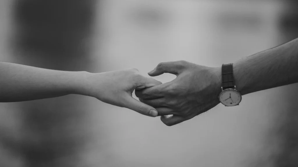 Dua tangan yang saling menggenggam namun mulai melepas, melambangkan makna lagu Back to Friends by SOMBR tentang kedekatan yang tak bisa dipertahankan.